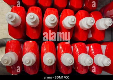 Rows of red dishwashing liquid bottles are placed neatly on a shelf in a store. The caps are white and the bottles are uniform in size and shape. This Stock Photo
