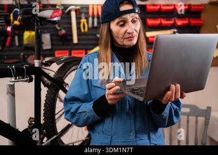 female mechanic with laptop. Female Bicycle Mechanic in workshop. copy space Stock Photo