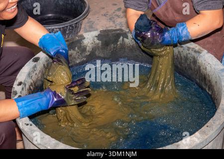 Thailand, Isaan, Sakon Nakhon, Donkoi Sustainable Village project, hands of women hand dyeing cotton thread in vat of natural indigo dye Stock Photo