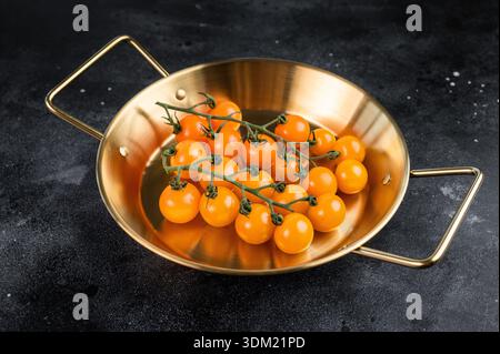 Ripe cherry tomatoes cluster in brass skillet on black rustic surface, top view food background with space for text. Stock Photo