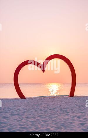 Romantic red love heart on sandy tropical beach with sunset sea reflection glow. Pastel sky evening. Valentine wedding couple travel vacation summer Stock Photo