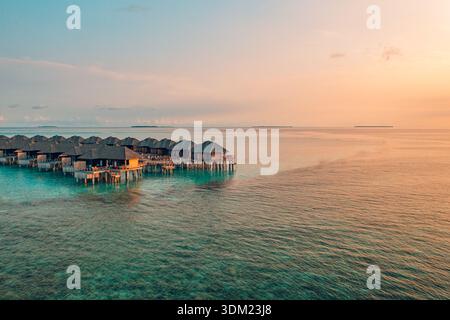 Radiant Maldives aerial overwater villas sunset warm golden sky stunning paradise coastal luxury resort travel destination romantic. Calm vacation art Stock Photo