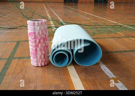 A pink and white foam roller sits next to a blue yoga mat. The mat is rolled up and placed on the floor Stock Photo