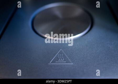 metal knob over hot surface warning, sleek stainless control dial embossed with heat triangle icon, cooltoned Stock Photo