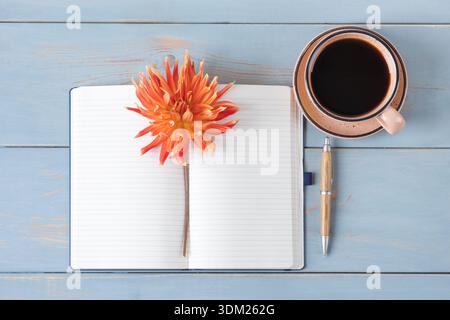 Top view of the desktop. Spiral notebook with an open blank page, pen, white cup with black coffee, dahlia flowers. Festive office desktop concept. Morning coffee cup. Stock Photo