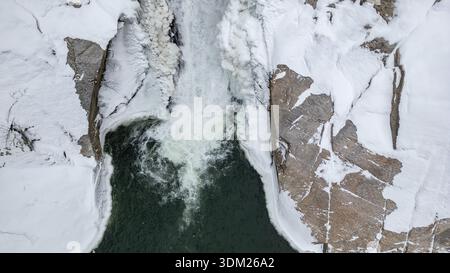 A snowy mountain with a large waterfall, surrounded by trees. Two people are standing near the waterfall, enjoying the beautiful scenery. Scene is cal Stock Photo