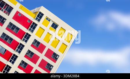Vibrant modern building facade with red and yellow geometric patterns at a diagonal angle against a clear blue sky, featuring copy space for creative Stock Photo
