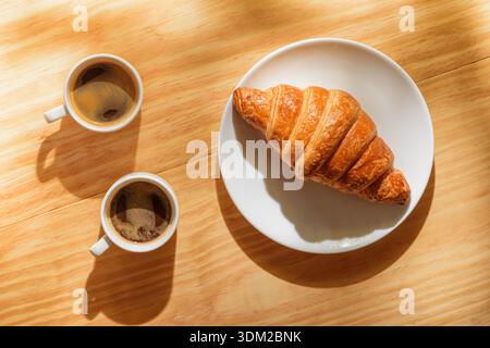 Two espresso cups and croissant in morning sun rays Stock Photo