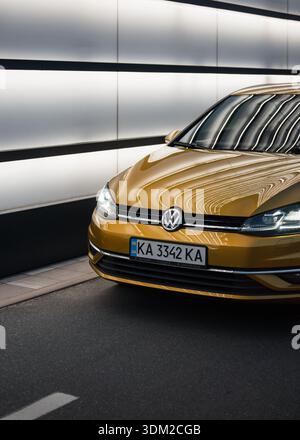 amber Volkswagen Golf on a street with white glowing wall. Front corner of modern VW hatchback car at night. Stock Photo