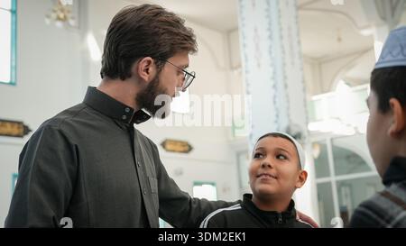Muslim children chatting and laughing with their teacher in mosque. Fasting Muslims worshipping and bonding at masjid during Ramadan. Religious educat Stock Photo
