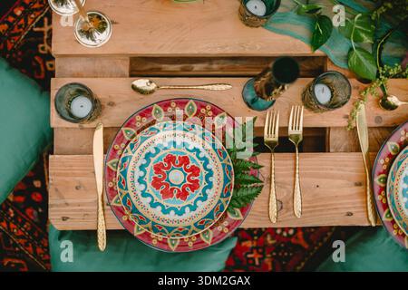 Boho table setting with plates, gold cutlery and candles on rustic wooden pallets Stock Photo