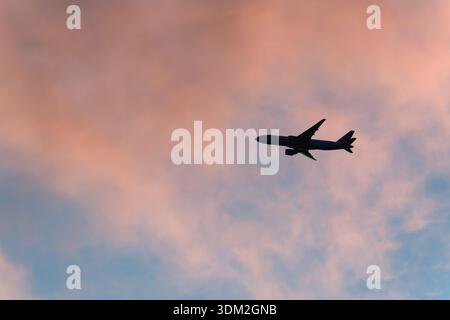 A silhouette of a passenger jet plane against pink clouds and blue sky at dusk Surrey England Stock Photo