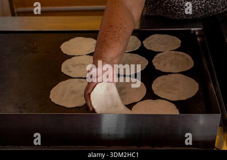 Traditional Mexican woman hand placing fresh corn tortillas on hot griddle comal authentic cooking. Stock Photo