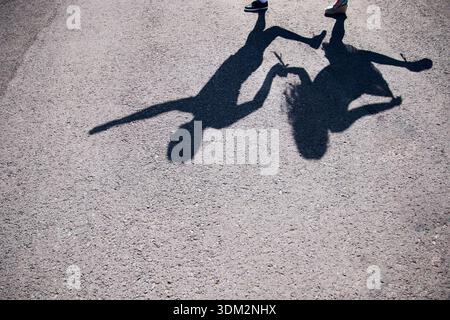 Leaping children form silhouettes against textured pavement background. Low setting sun cast shadows of kids playing on rugged stone floor with Stock Photo