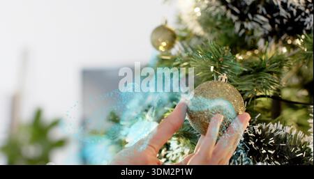 Placing hands arranging glittery gold ornament on faux green tree at home with blue particle light Stock Photo