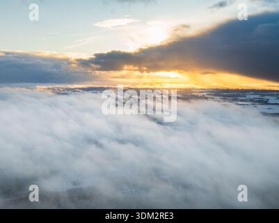 Breathtaking drone view of golden sunset sunbeams breaking through dramatic clouds over snowy winter landscape and frozen lakes in Finland. Stock Photo