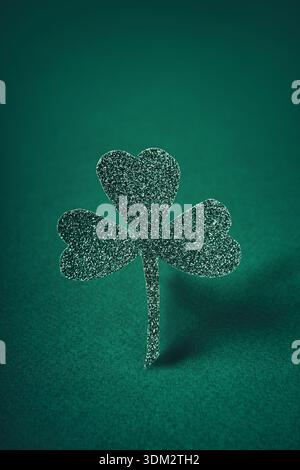 Glittering shamrock standing on green felt background, symbolizing luck and celebration Stock Photo
