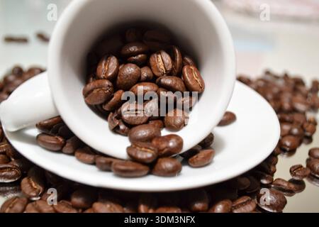 Coffee beans spilling from white cup on saucer Stock Photo