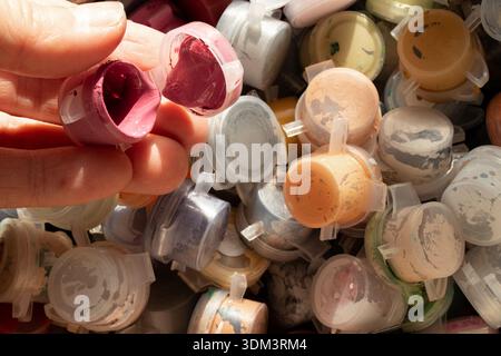 An artist's hand holding open paint containers among many paint jars, drawing and hobbies Stock Photo