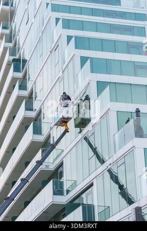 Worker on hydraulic lift cleaning windows of modern glass building with balconies Stock Photo
