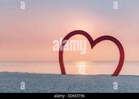 Heart shape drawn in beach sand with ocean sunset view romantic love symbol serene waves horizon colorful sky summer travel background Stock Photo