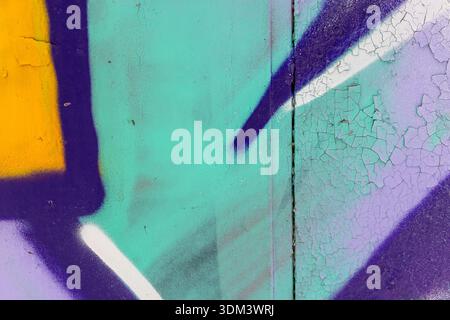Vibrant graffiti fragment on a weathered wall featuring bold purple, teal, and yellow panels. Cracked paint adds texture and depth, capturing urban en Stock Photo