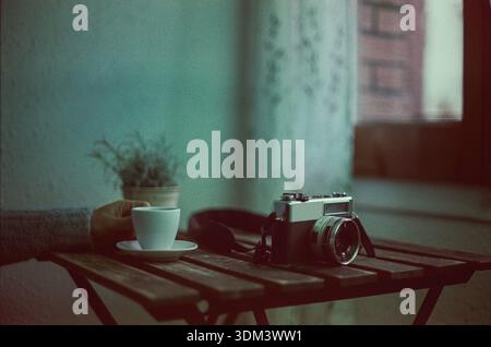 Image with vintage film of hands holding a cup of coffee on a rustic table and an analog camera. Stock Photo