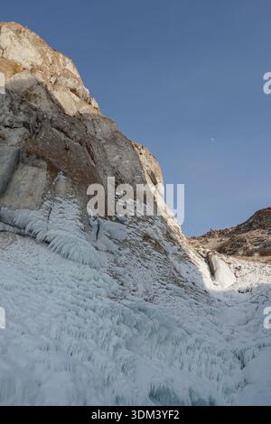 Frozen rock cliff covered with thick ice formations and icicles rises against a clear blue winter sky Stock Photo