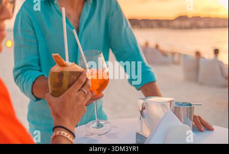 Couple cheering with cocktails sunset ocean beach view vibrant optimism cloud dancer color trend 2026 slow travel romantic mood Stock Photo