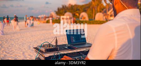 DJ playing music beach party sunset mood tropical nightlife crowd dancing seaside celebration travel destination Stock Photo