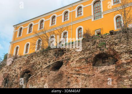 A bright yellow modern building stands atop layers of weathered red brick ruins in Istanbul. Stock Photo