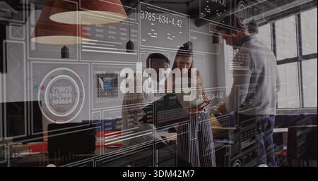 Analyzing three-person team in business attire examining laptop and tablet at open office, with HUD Stock Photo