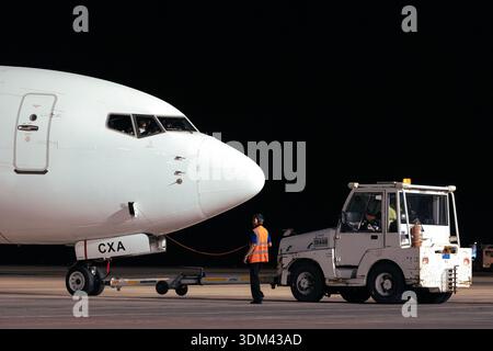 Aircraft pushback operation at night with ground crew and tow tractor Stock Photo
