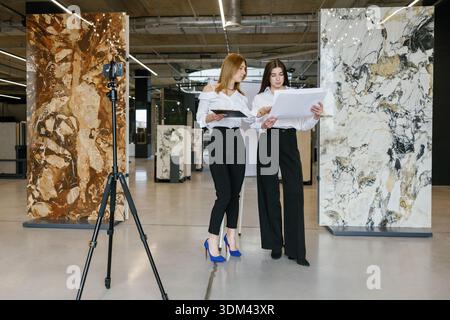 Professional female architects collaborating on interior design project, planning using blueprints in a modern marble and tile showroom Stock Photo