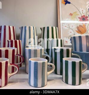 Collection of colorful striped ceramic coffee mugs with handles in burgundy red blue gray green white vertical stripes pattern close up display on whi Stock Photo
