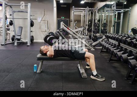Man doing dumbbell press on bench at commercial gym Stock Photo