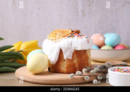 Delicious Easter cake with sprinkles, painted eggs, willow branches and tulips on table against gray background, closeup Stock Photo