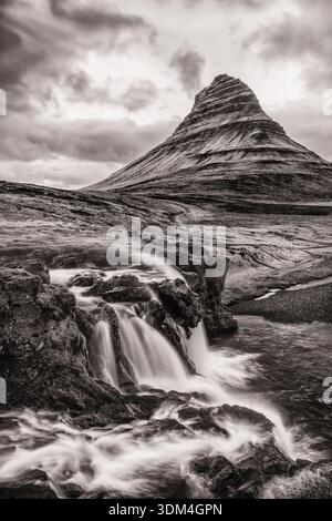 A waterfall blows up the cliff on a windy day at Kirkufellsfoss, with iconic Kirkufell Mountain behind, on Snaefellsnes Peninula, Iceland. Stock Photo