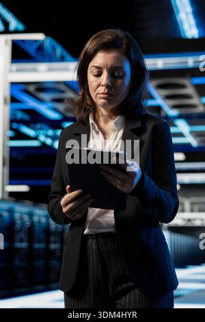 Data center software developer using tablet to install and configure equipment hosting digital services. Server farm specialist using device to test and repair mainframes managing file transfers Stock Photo