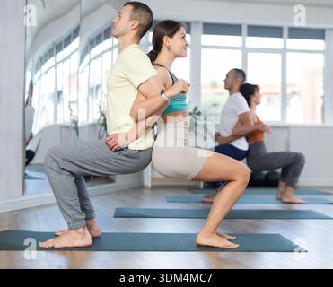 Group of men and women doing acroyoga exercises in pairs, exercising partner yoga during training in fitness center Stock Photo