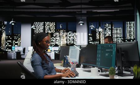Female programmer using large language model application to get help with coding tasks. African american woman interacting with AI LLM chatbot PC GPT software on PC Stock Photo