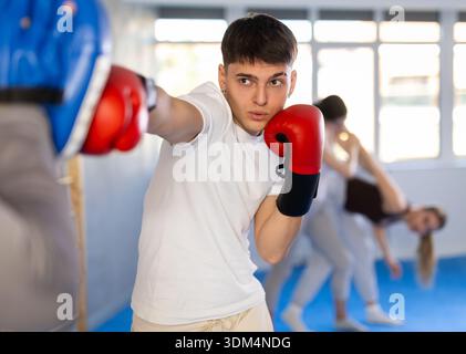 Guy masters boxing strikes on the trainer punch mitts during training Stock Photo