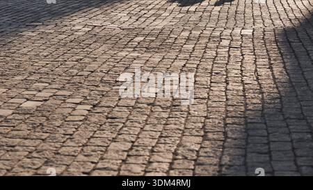 Cobblestone street surface with shadows creating abstract lines on old pavement Stock Photo