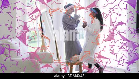Sharing two women in bathrobes with headbands passing skincare jars in sunlit lounge near mirror Stock Photo