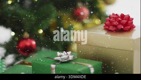 Displaying stack of wrapped gift boxes sitting on home table near decorated evergreen, with red bow Stock Photo