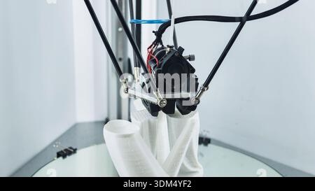 3D printer nozzle creating a white prototype object on a build plate Stock Photo