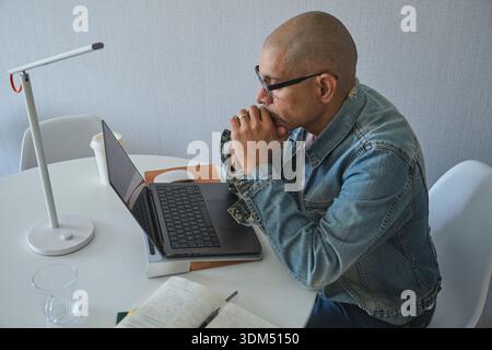 Bald man working remotely, concentrating on laptop research and problem-solving Stock Photo