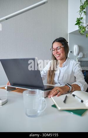 Smiling woman sitting at desk using laptop for remote work Stock Photo