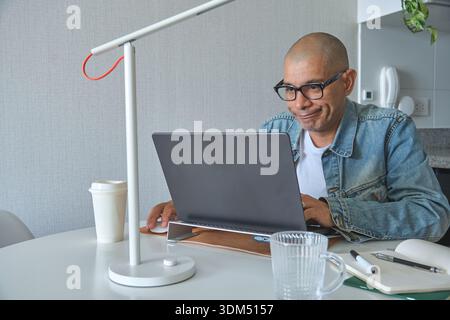 Man smiling at laptop screen while working at home with a desk lamp and coffee Stock Photo