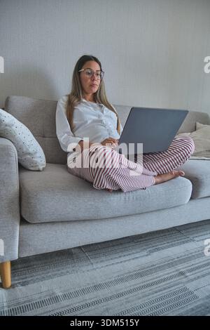 Pregnant woman using a laptop on a sofa, comfortable at her home office Stock Photo